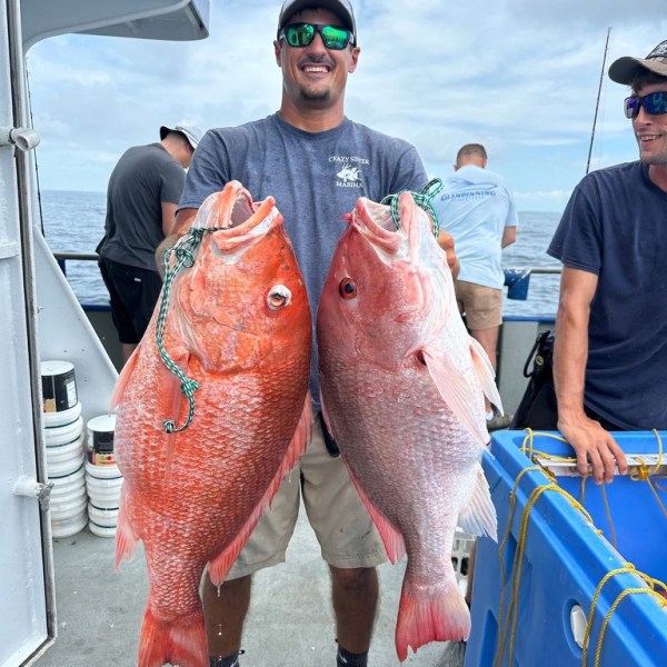 Man holding two large red fish on a boat with others in the background.