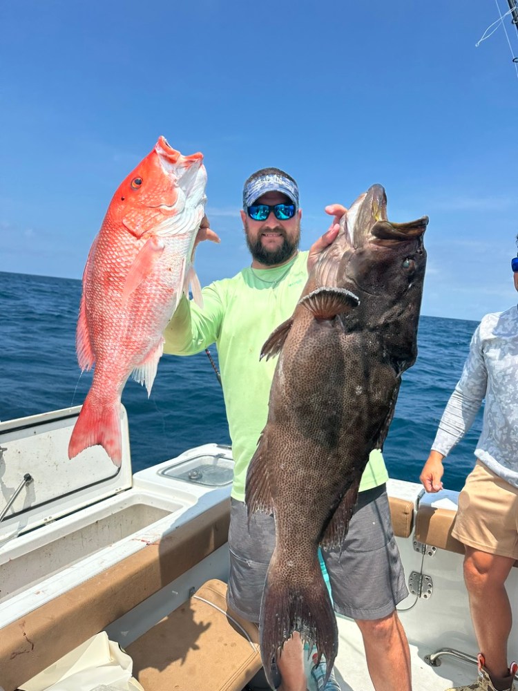 Man on boat holding large red and black fish against a blue sky backdrop.