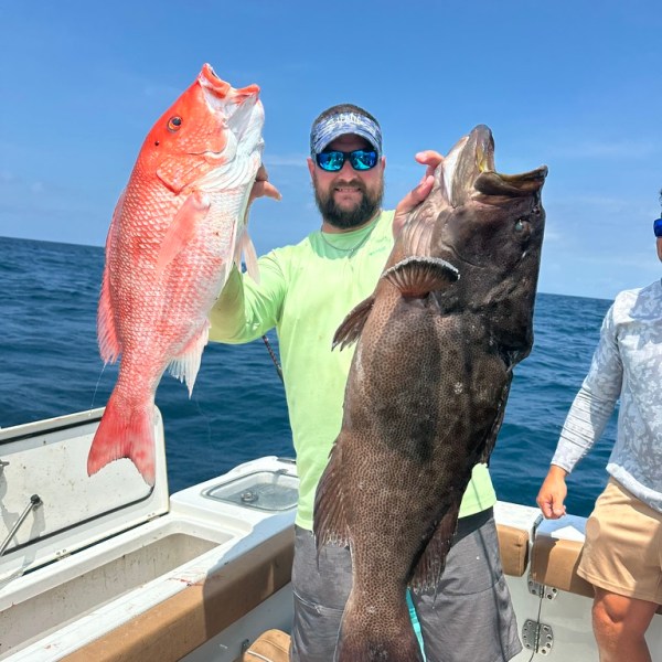 Man on boat holding large red and black fish against a blue sky backdrop.