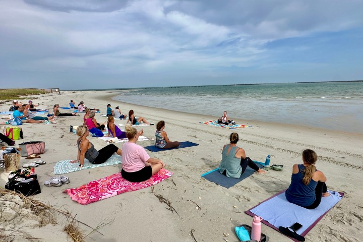 Group of people doing yoga on a sandy beach by the ocean.