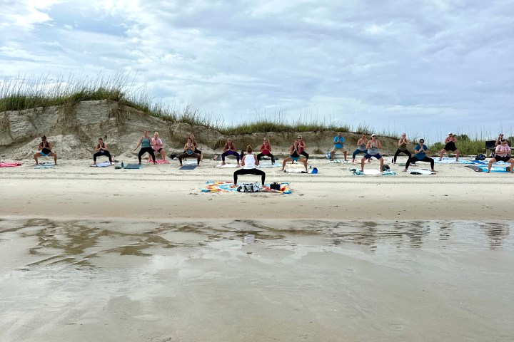 Group doing yoga on a sandy beach under a cloudy sky.
