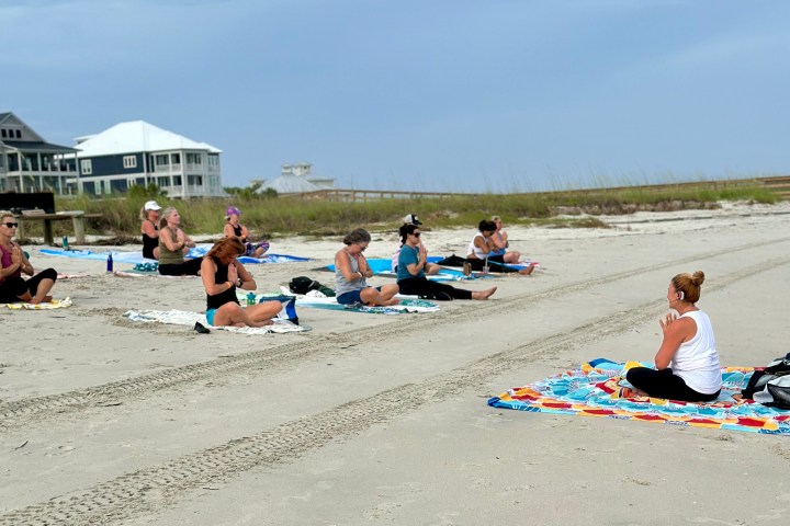 People practicing yoga on a sandy beach on a cloudy day.