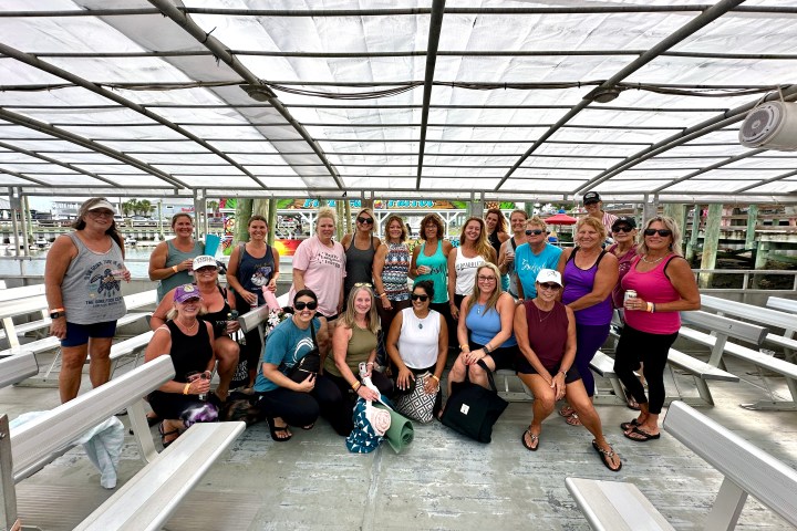 Group of people posing under a canopy on a boat with benches.