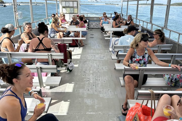 People sitting under a canopy on a boat, holding drinks and enjoying the sea view.