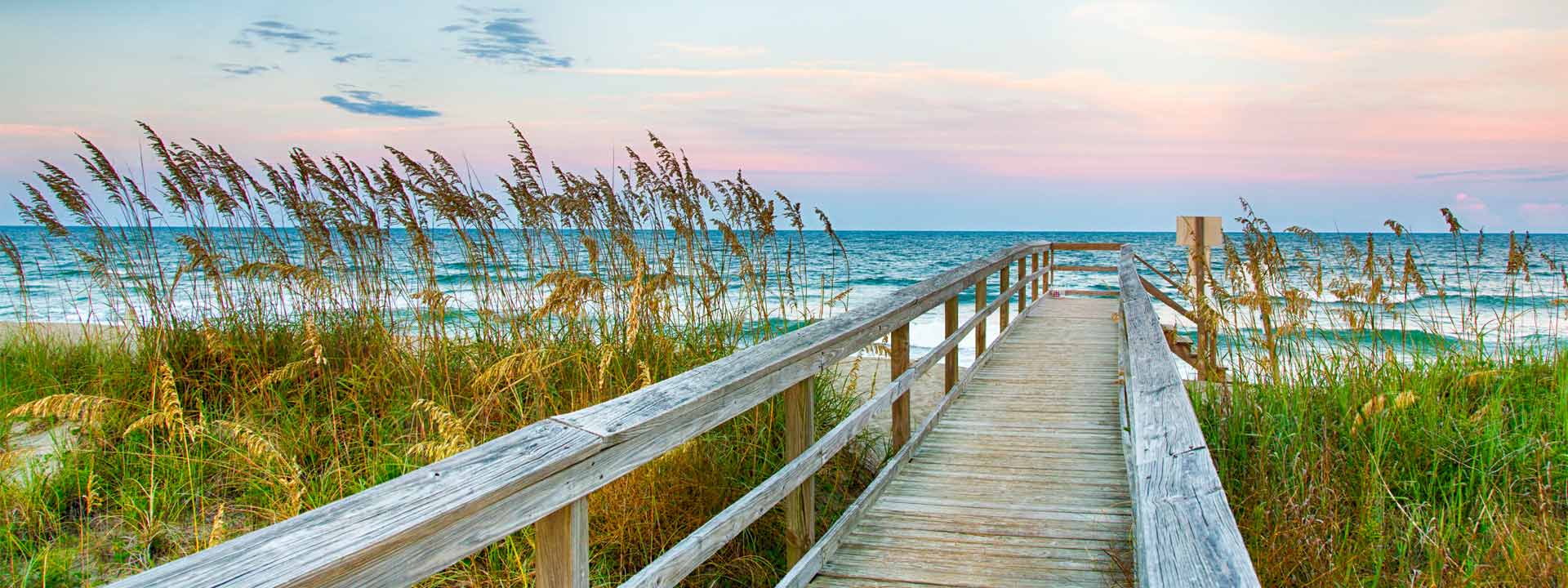 Fall in Myrtle Beach Wooden walkway leading to beach with sea oats, ocean waves, and pastel sky.