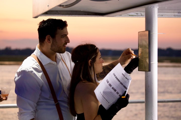 Two people reading a notice on a boat at sunset, holding papers and a flashlight.