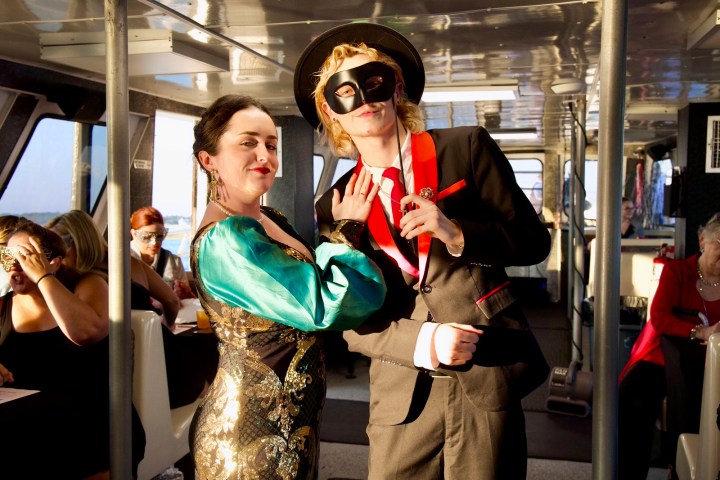 Two people in costumes at a masquerade party on a boat, surrounded by other guests.