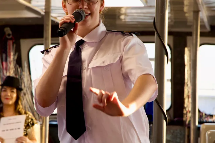Person in captain's uniform speaking into a microphone inside a boat.