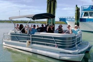 Group of people on a pontoon boat in a harbor, with another boat in the background.
