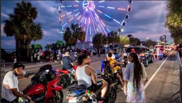 Screenshot_8-9-2025_161435_www.bing.com Night street scene with motorcycles, people, and a lit Ferris wheel in the background.