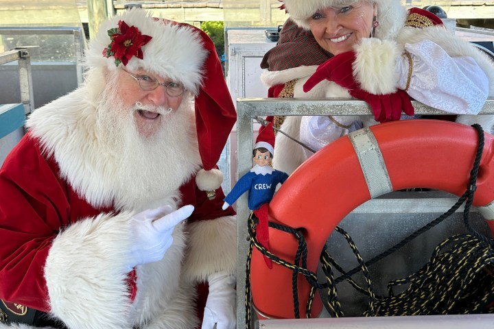Santa and Mrs. Claus smiling with an elf doll and lifebuoy on a boat.
