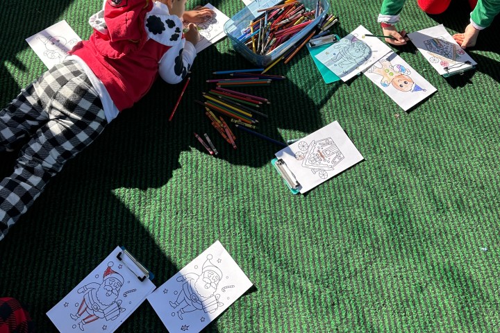 Children coloring on a green carpet with holiday-themed sheets and colored pencils.