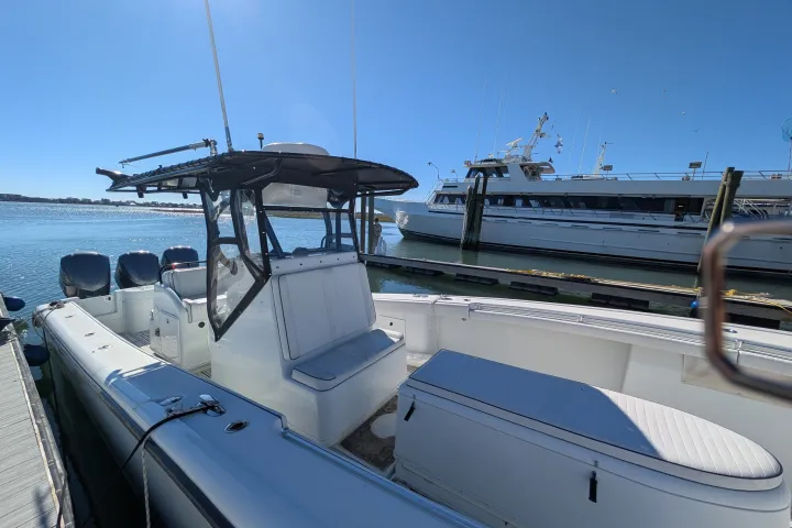 View of a motorboat docked at a harbor with yachts in the background under a clear blue sky.