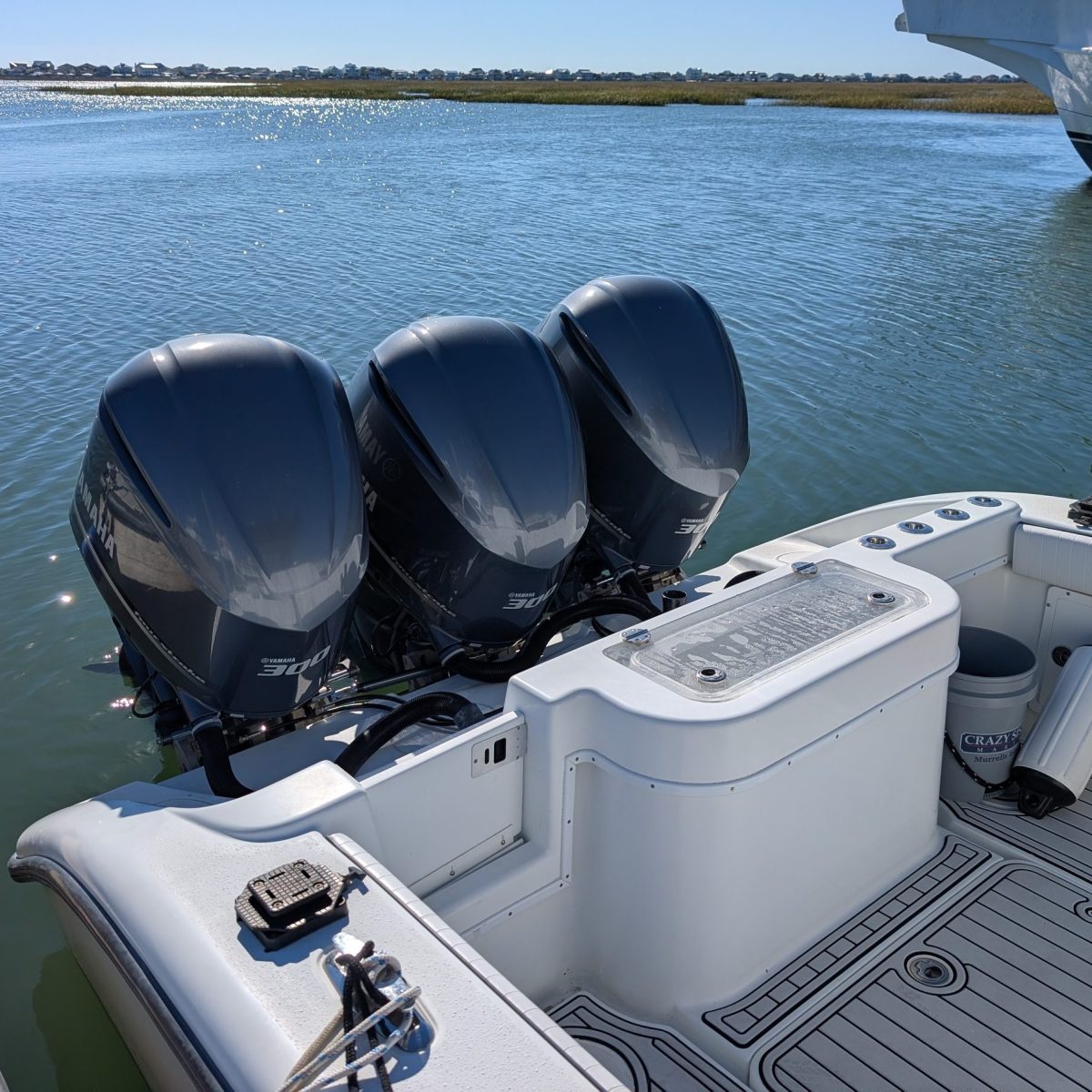 Boat with three outboard motors docked in a calm water marina under clear blue sky.