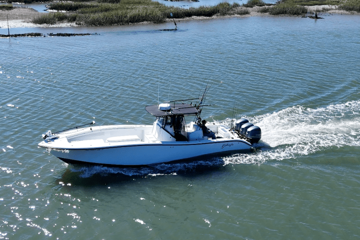 A motorboat traveling through water, with grassy marshland in the background.