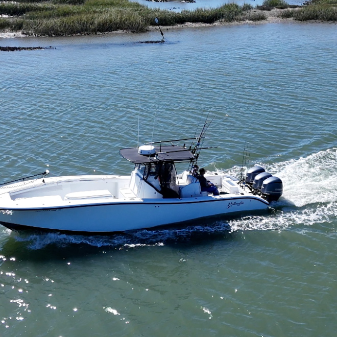 A motorboat traveling through water, with grassy marshland in the background.