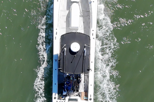 Aerial view of a white motorboat with three outboard motors traveling on green water.