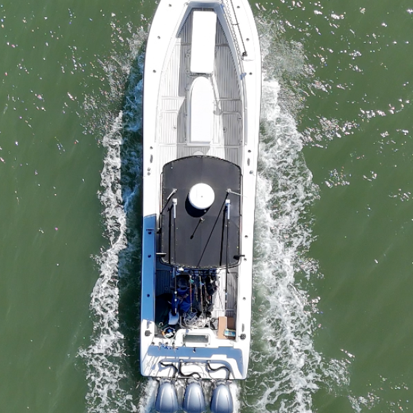 Aerial view of a white motorboat with three outboard motors traveling on green water.