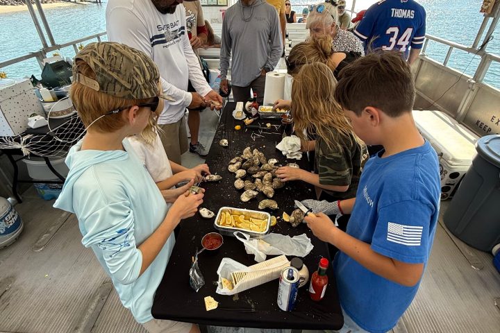 People gathered around a table on a boat shucking oysters and enjoying a casual gathering.