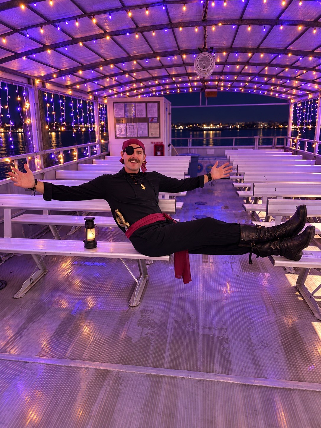 Person in pirate costume posing on a boat with purple lights.