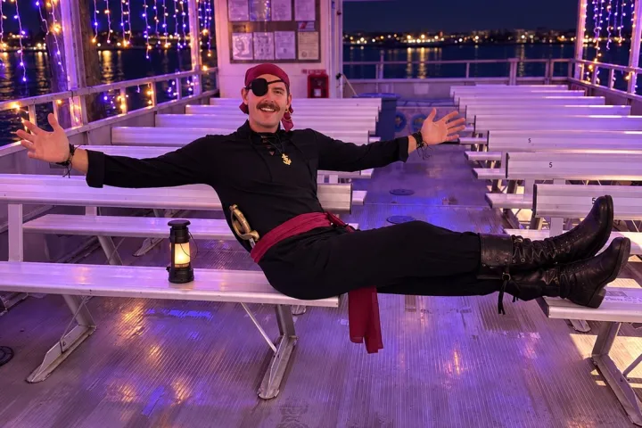 Person in pirate costume posing on a boat with purple lights.