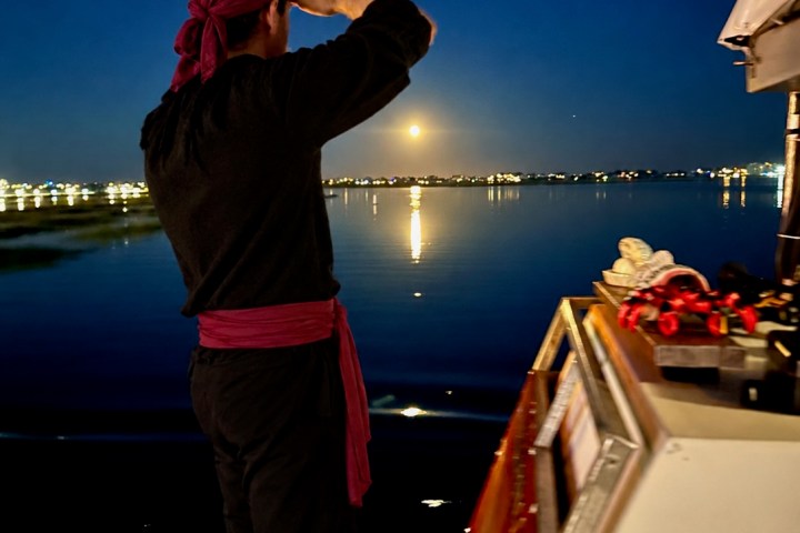 Person in pirate attire gazing at night skyline over calm water from boat.