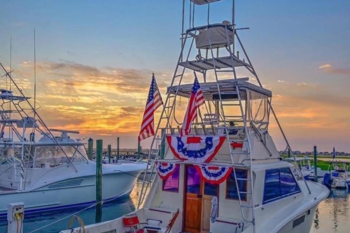Fishing boat decorated with American flags and banners at sunrise in a marina.