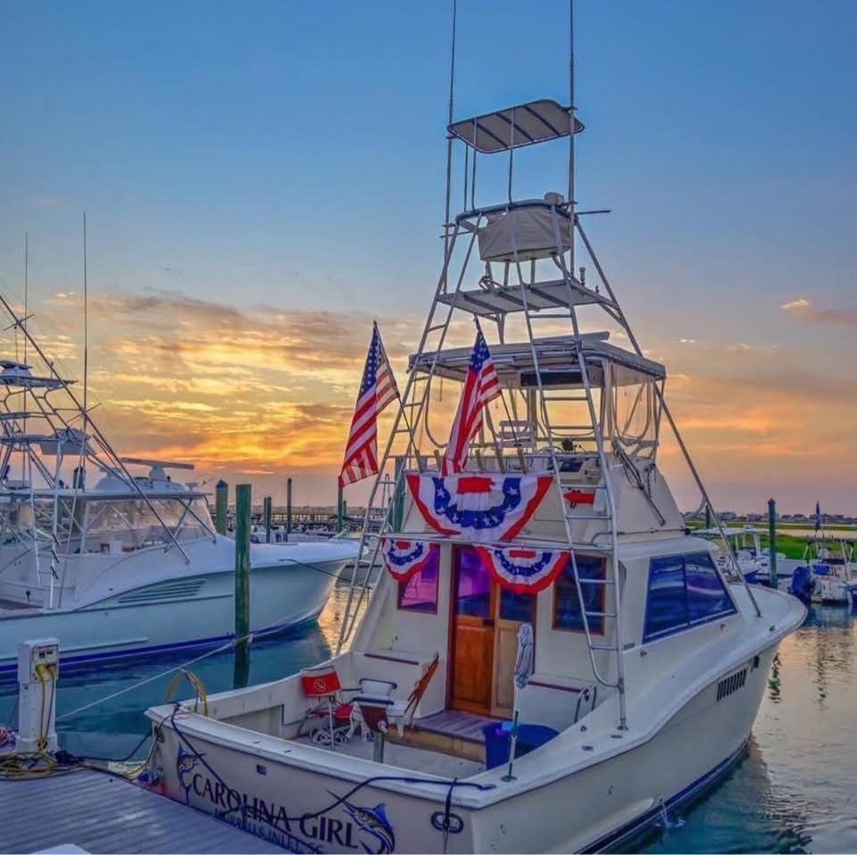 Fishing boat decorated with American flags and banners at sunrise in a marina.