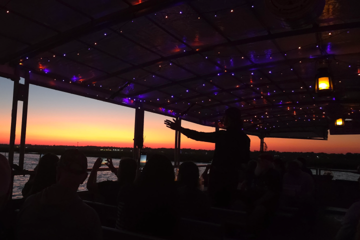 People on a boat at sunset with string lights above.
