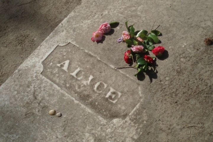 Gravestone with 'Alice' engraved, flowers and shells placed on top.