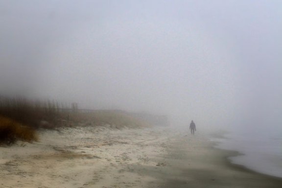 Person walking on a foggy beach with blurred surroundings and sea waves.