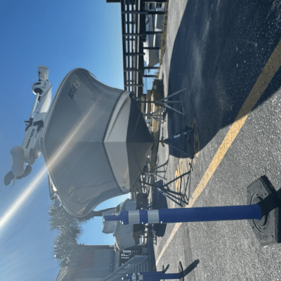 Boat on trailer in parking lot with clear sky and lens flare.
