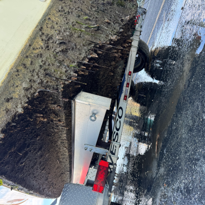 Boat hull covered in barnacles on a trailer, next to wet pavement.