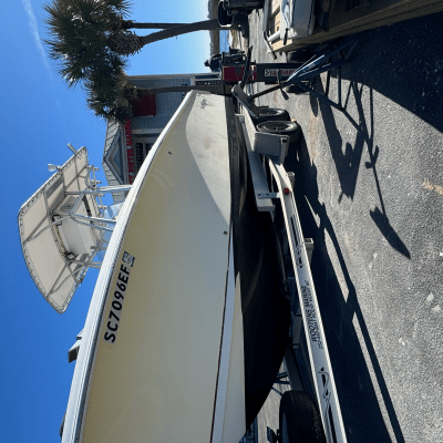 Boat on trailer with a palm tree and building in the background under a clear blue sky.
