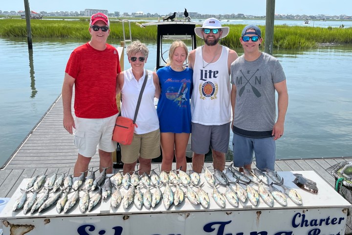 Group of five people on a dock with many fish displayed on a table labeled 'Silver Tuna Charter Boat'.