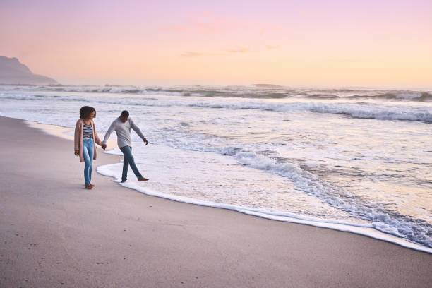 Couple holding hands walking along a beach at sunset.