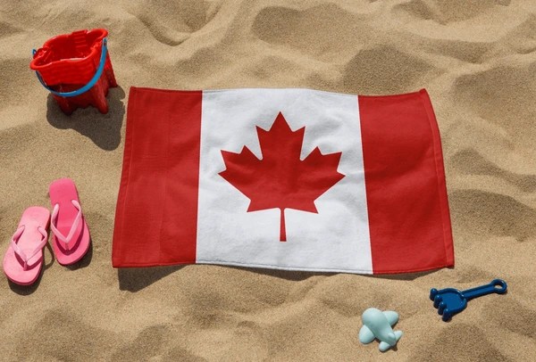 Canada flag on sandy beach with pink sandals, red bucket, and blue shovel.