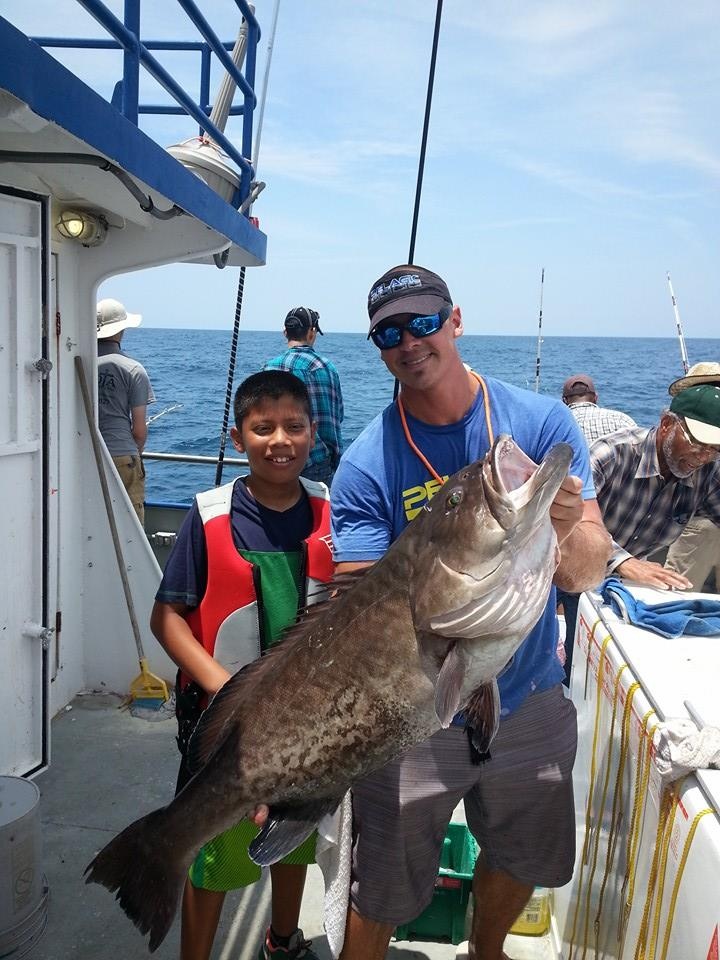Two people on a boat holding a large fish, with the ocean in the background.