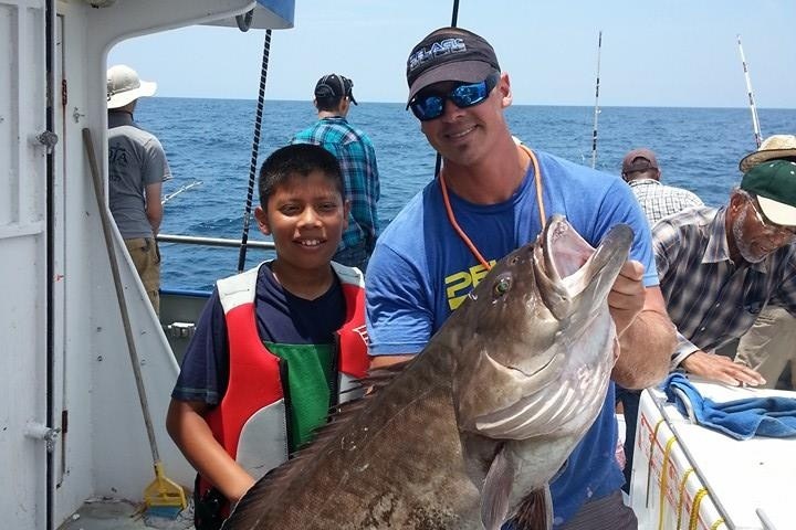 Two people on a boat holding a large fish with other people in the background.