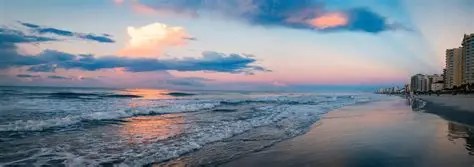 Beach at sunset with colorful sky and buildings along the shoreline.