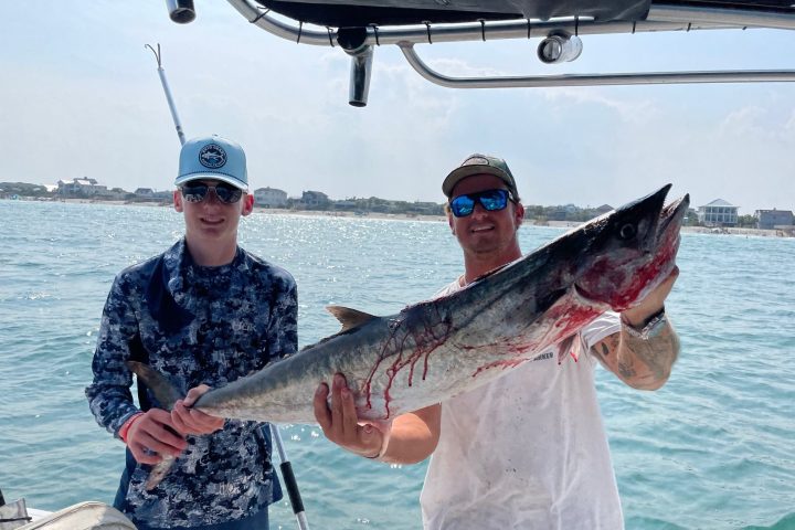 Two people on a boat holding a large fish with the sea in the background.