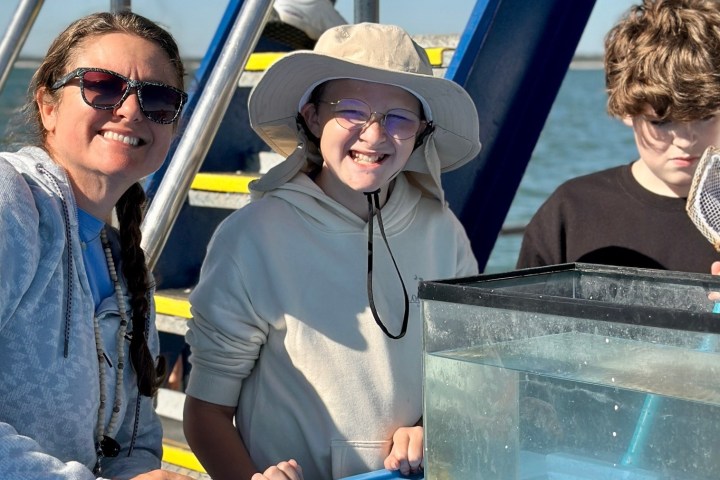 Three people on a boat smiling next to a fish tank with a net.