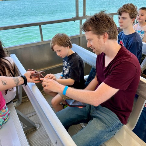 Man and children on a boat interacting with a small sea creature.