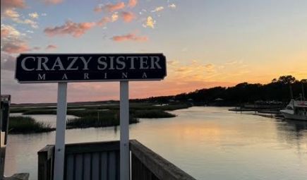 Sign reading 'Crazy Sister Marina' at sunset over a calm river.