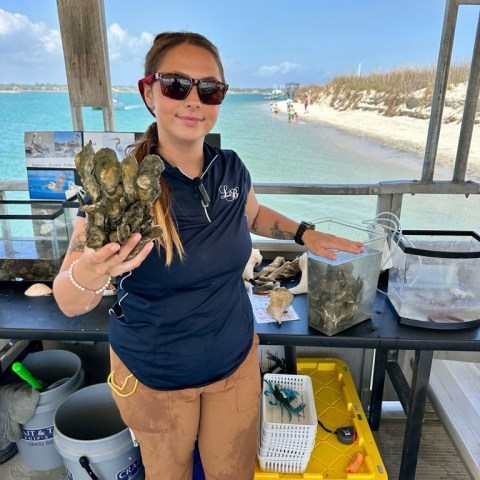 Person holding shellfish at a beachside research station with ocean background.