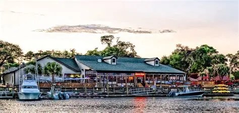 Lakeside restaurant with boats docked, trees in background.