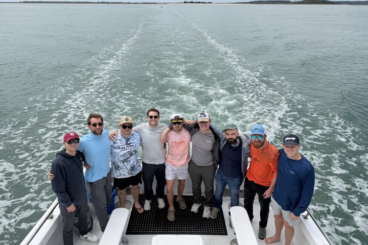 Group of men posing on a boat with ocean in the background.