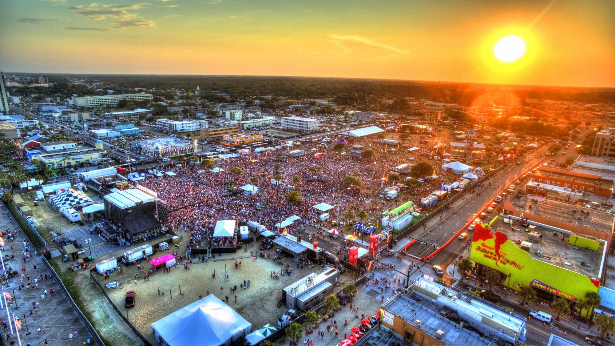 Aerial view of a bustling outdoor music festival at sunset.