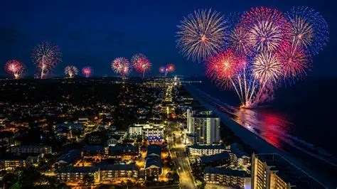 Aerial view of beach cityscape with bright fireworks in the night sky.