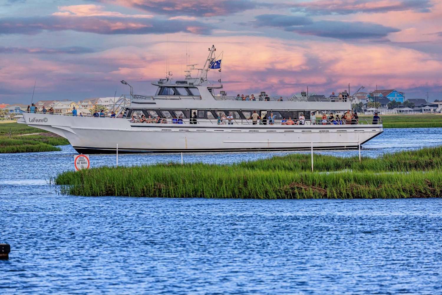 White boat with passengers on a river at sunset.